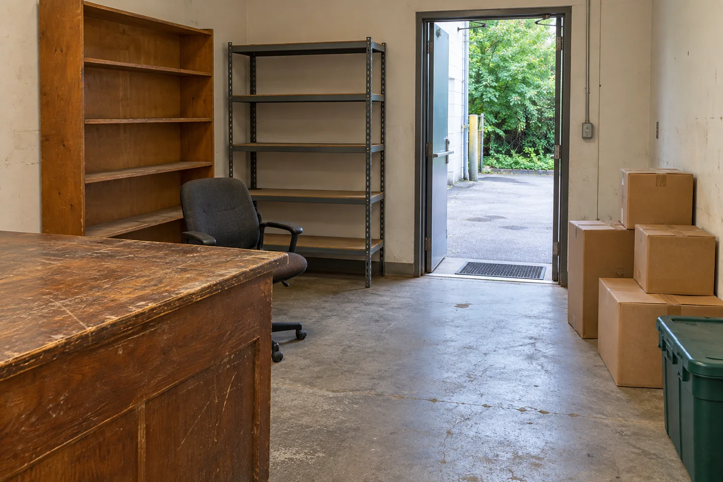 Used shelving, a counter, chair and cartons beside a clear business loading route.
